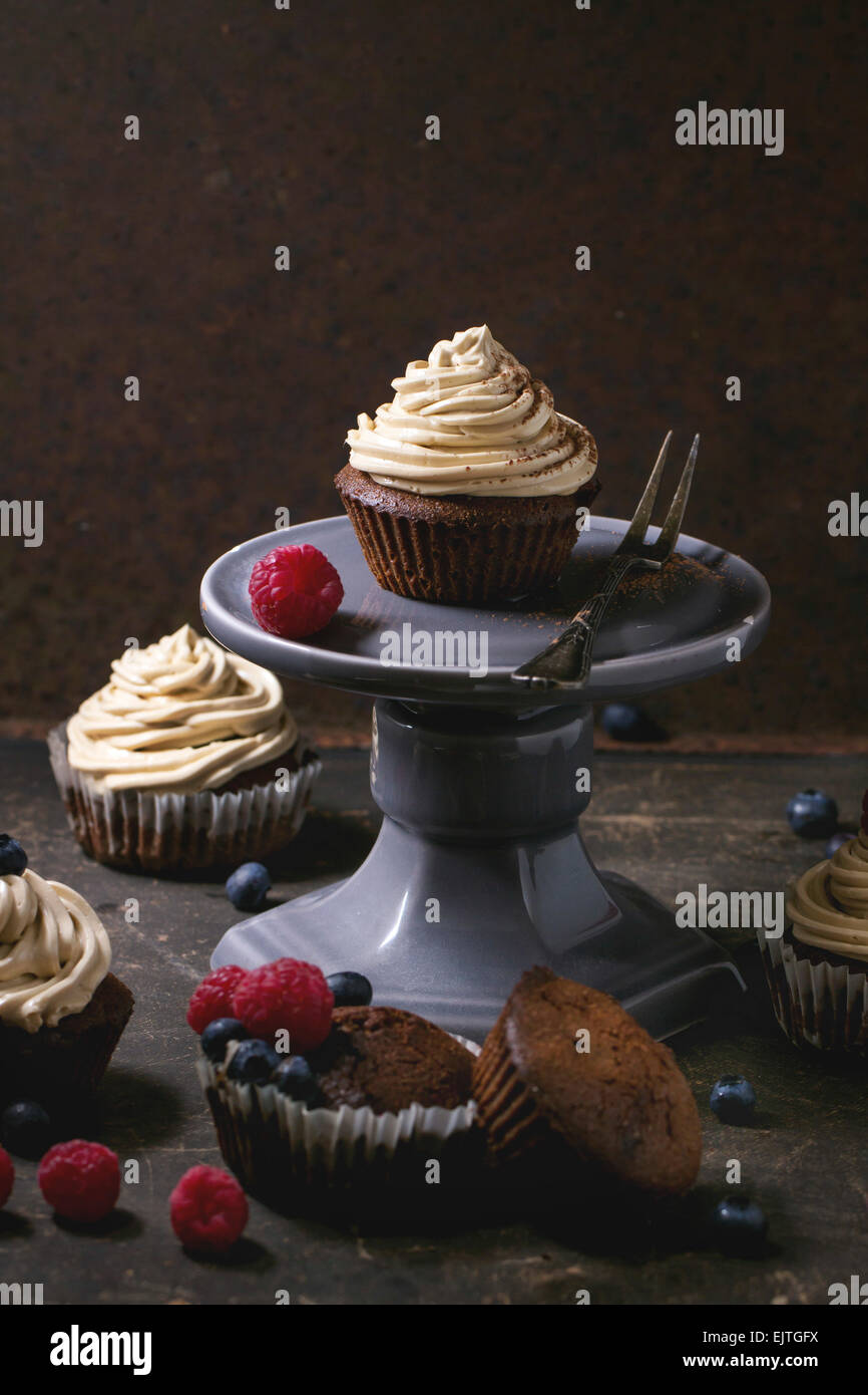 Chocolate cupcakes with butter coffee cream and fresh berries over dark background Stock Photo