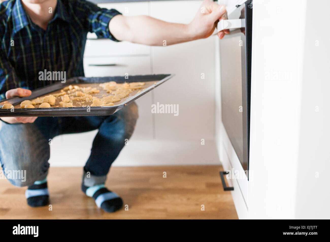 Low section of man putting baking tray in oven Stock Photo