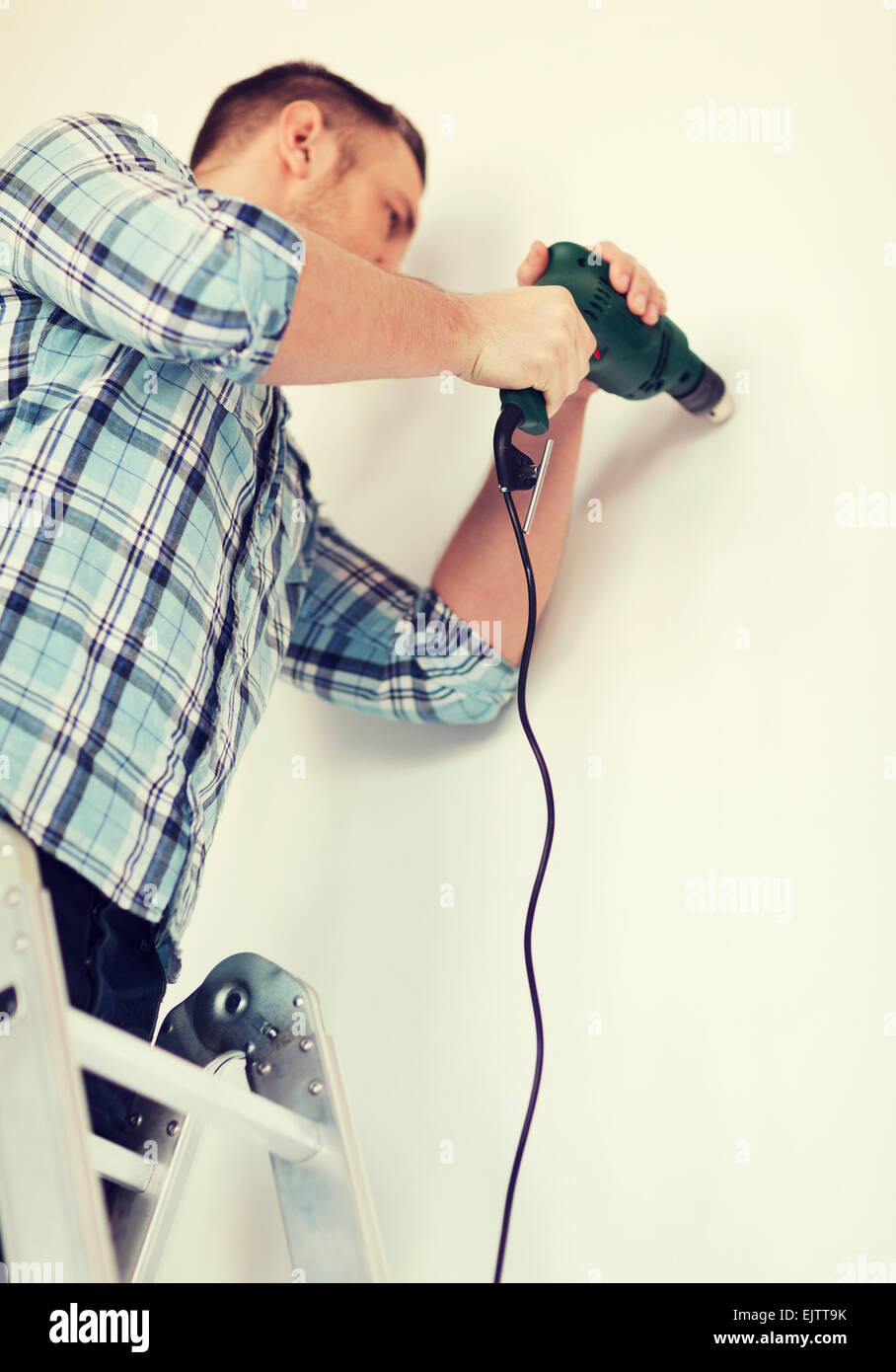 man with electric drill making hole in wall Stock Photo