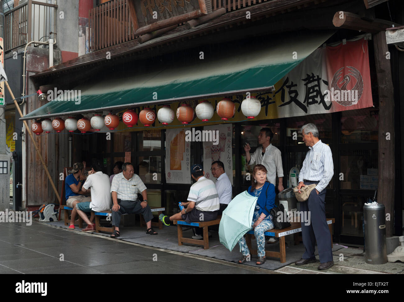 Visitors rest outside a shop on Konpira Ometesando Street on a rainy day, Kotohira, Shikoku, Japan Stock Photo