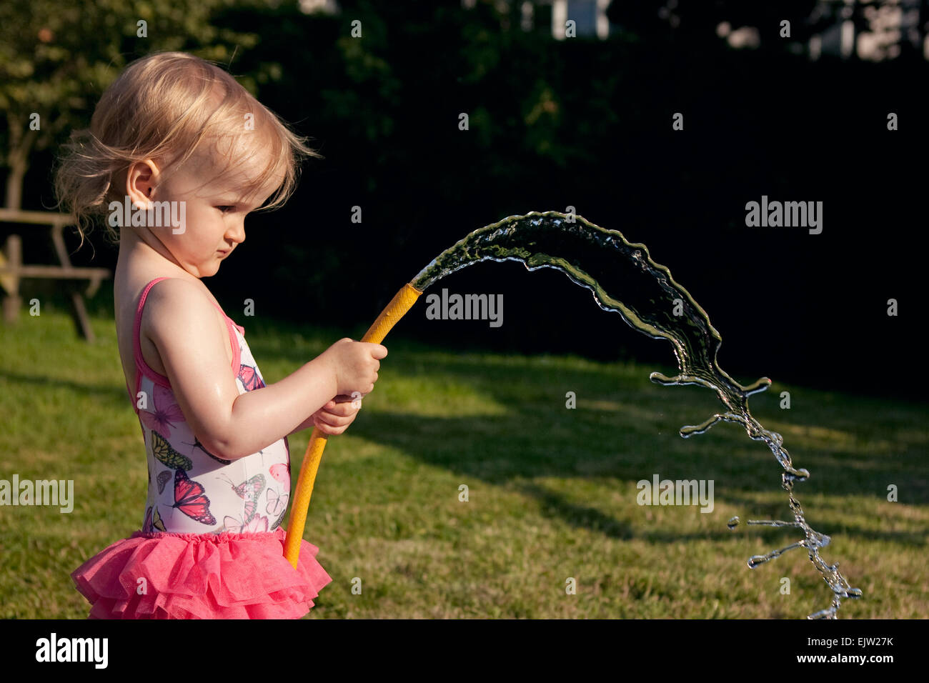 Young girl spraying water from a hosepipe in the garden in summer. Stock Photo
