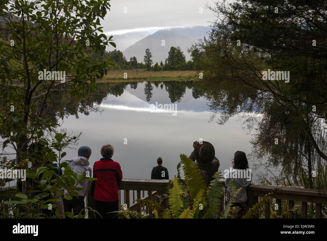 Visitors looking at reflections of Aoraki/Mk Cook at Lake Matheson, Fox Glacier, South Island, New Zealand Stock Photo