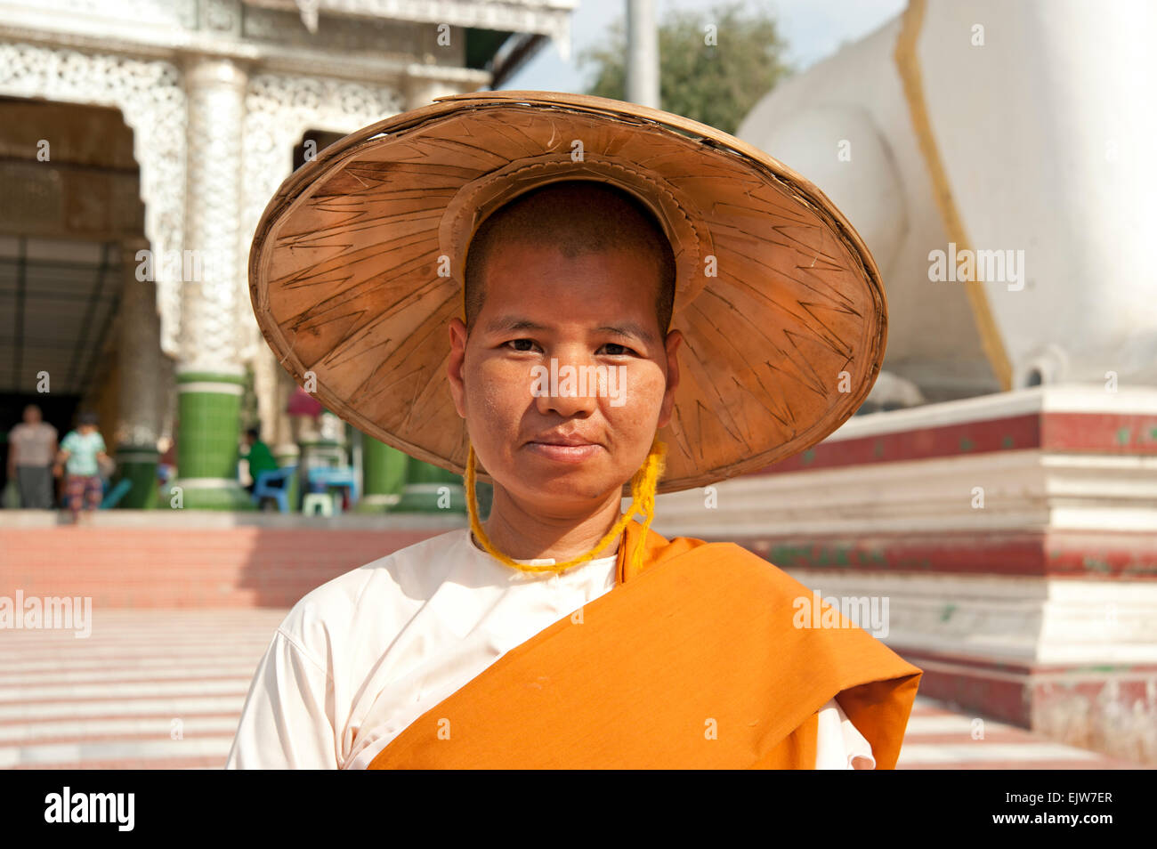 Portrait of a Buddhist nun wearing a wide brimmed straw hat in front of a Buddhist temple Mandalay Myanmar Burma Stock Photo