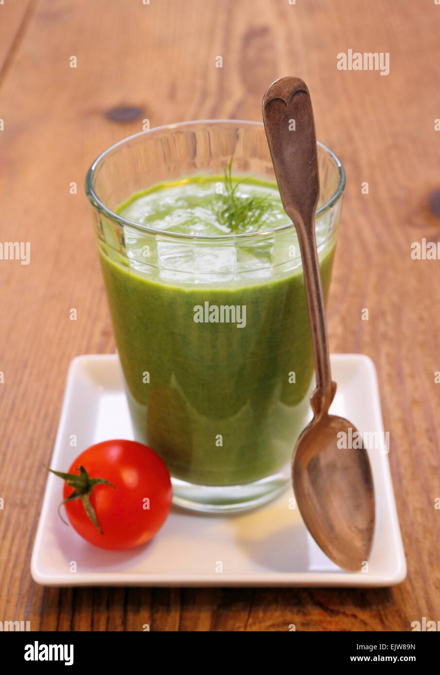 Green spinach smoothie and small red tomato, wooden background Stock Photo