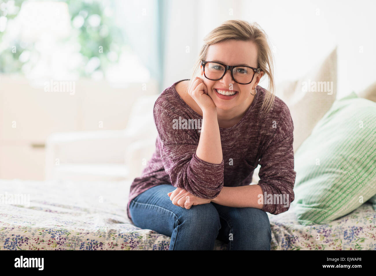 Portrait of smiling young woman sitting on bed Stock Photo - Alamy