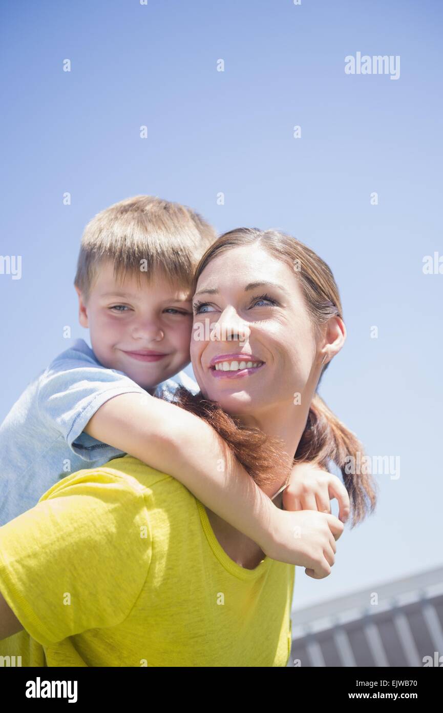 Happy mother giving her son a piggyback ride in the city stock photo