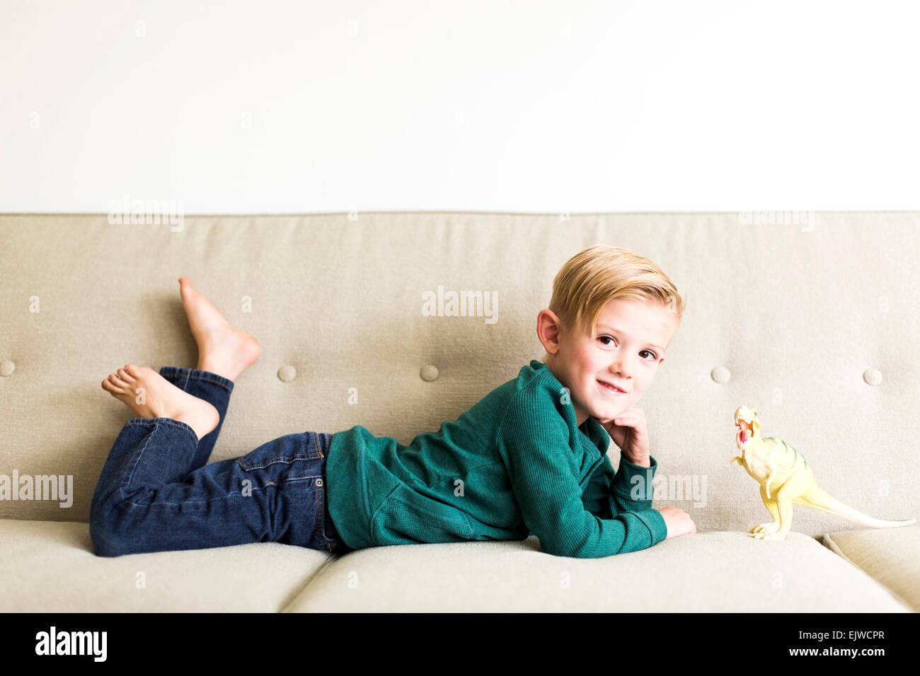 Boy (2-3) lying on sofa with toy dinosaur Stock Photo