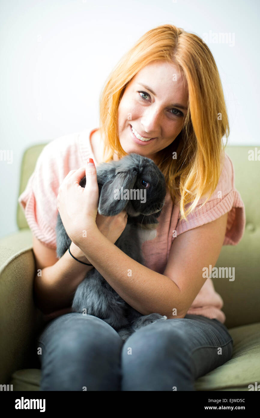 Woman sitting on sofa embracing rabbit Stock Photo - Alamy