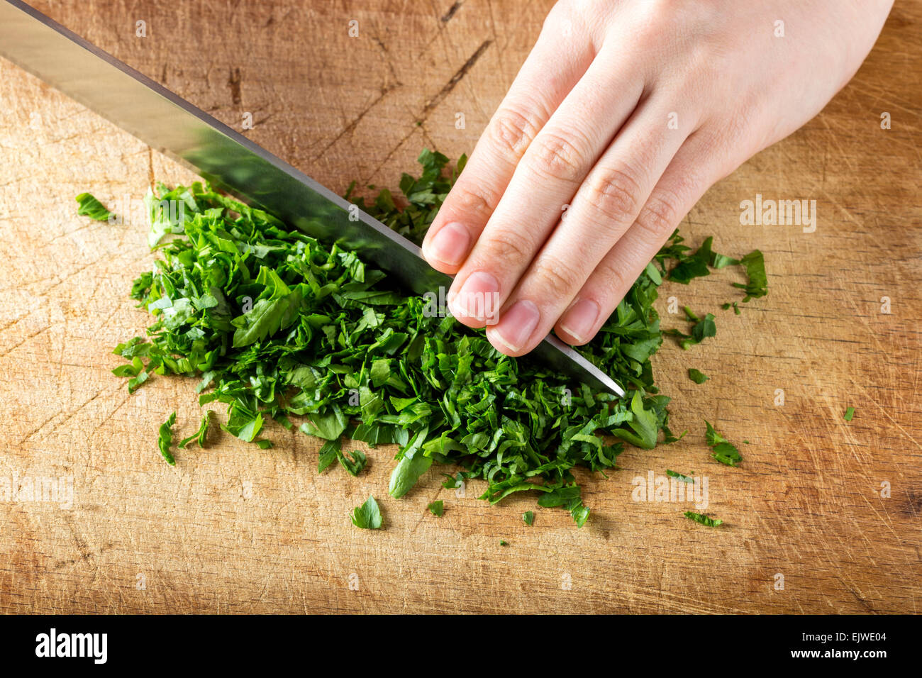 Female hands chopping fresh parsley on wooden board Stock Photo