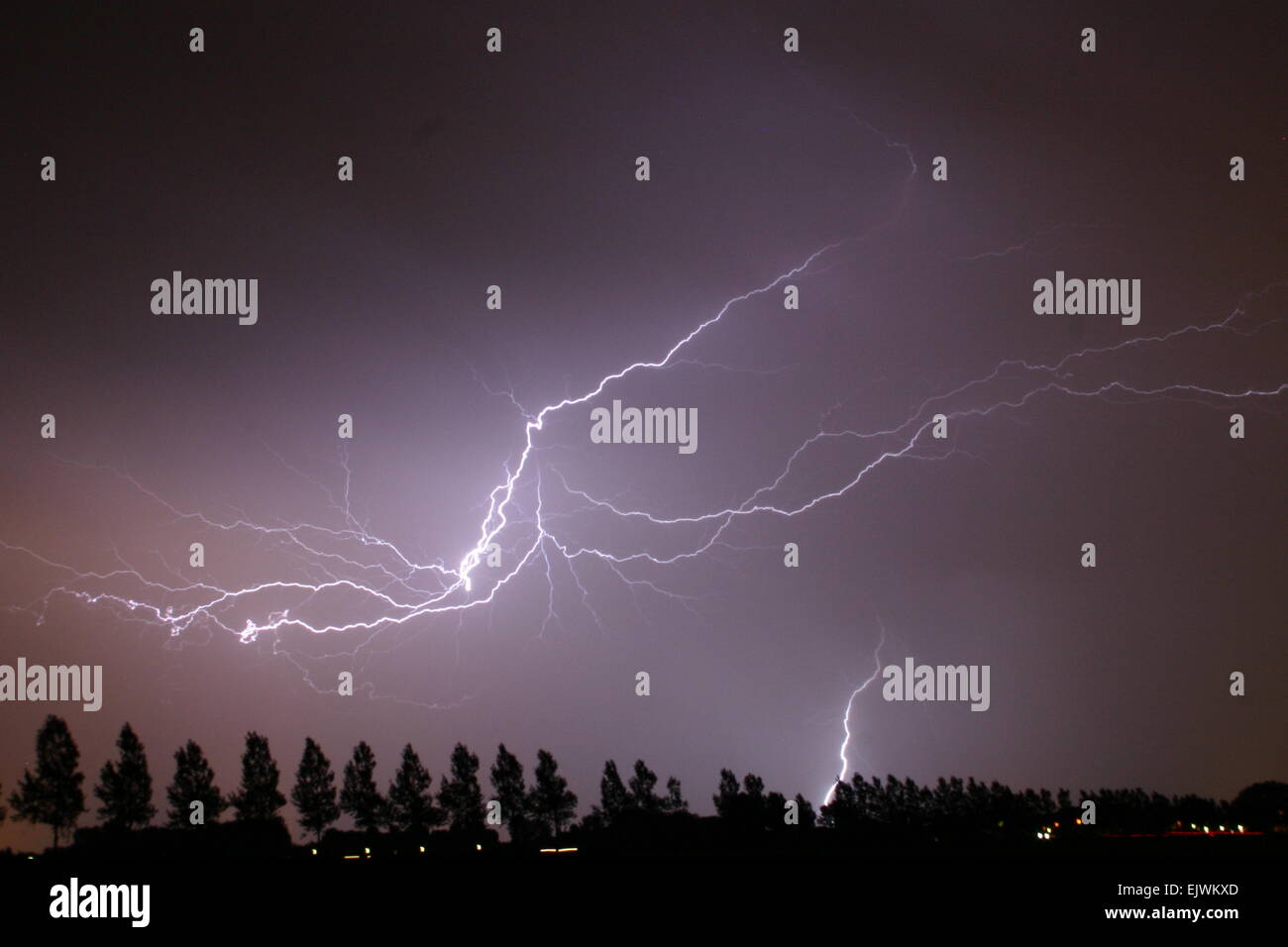 Severe lightning strikes close by causing a purple color in the clouded sky. Stock Photo