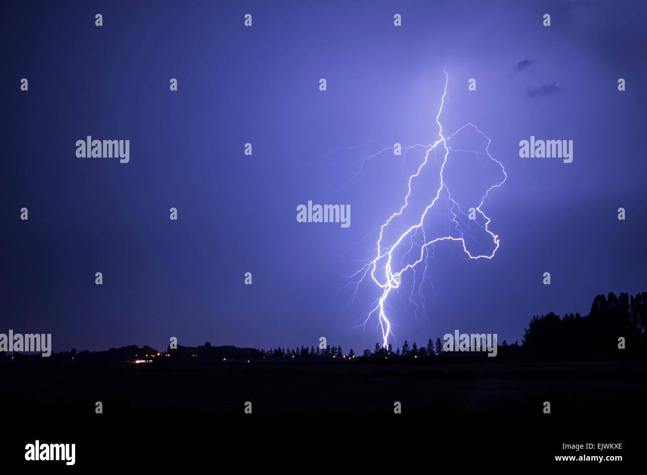 Lightning strikes close by causing a purple color in the clouded sky. Stock Photo