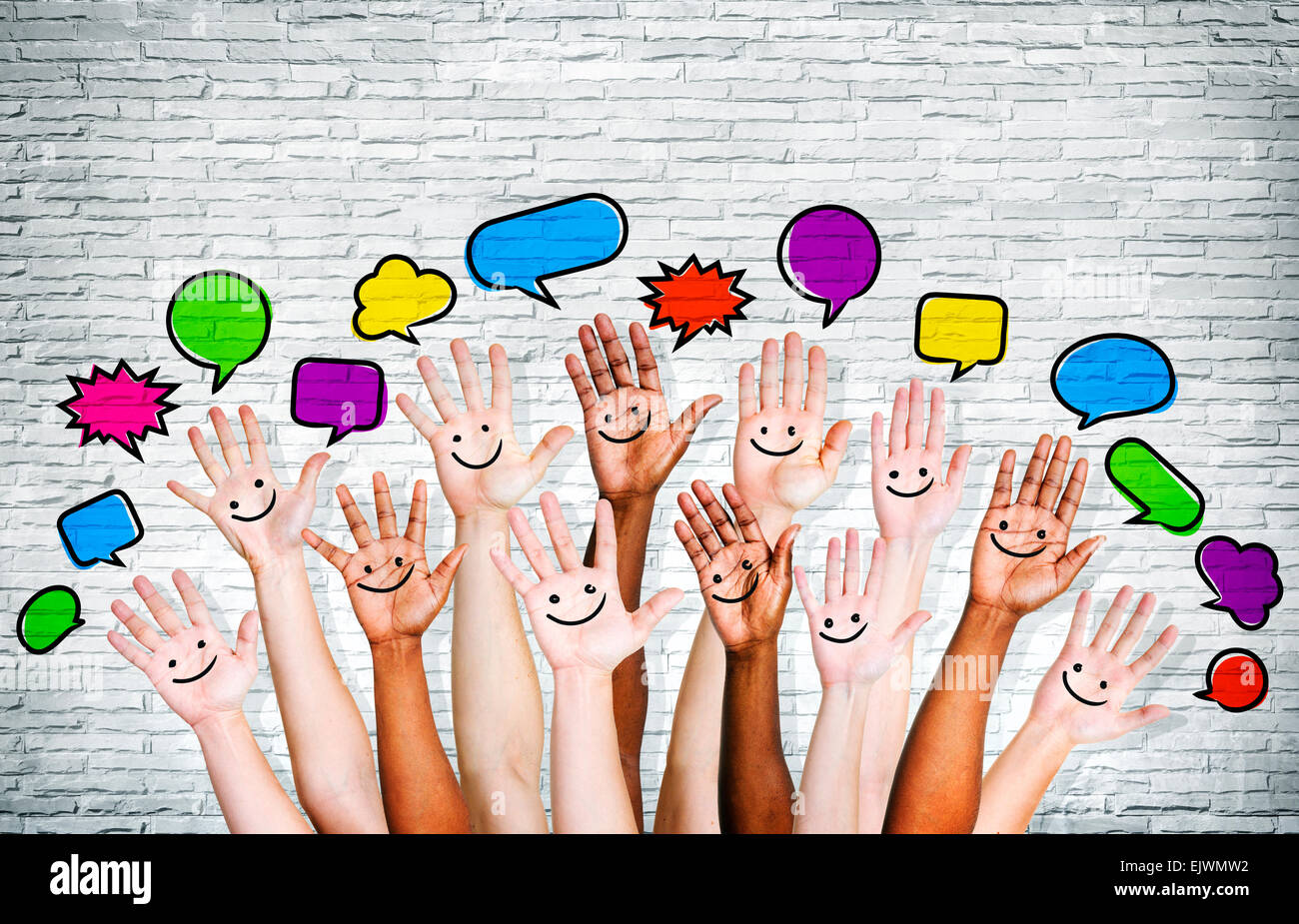 Multi ethnic people's hands raised with speech bubble by brick wall. Stock Photo