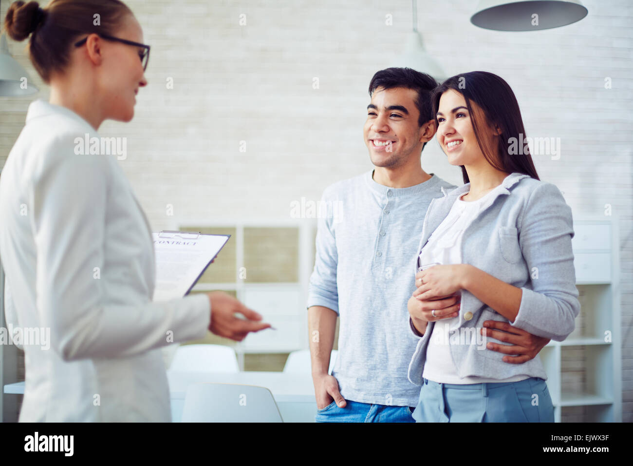 Young couple listening to female agent in realtor office Stock Photo