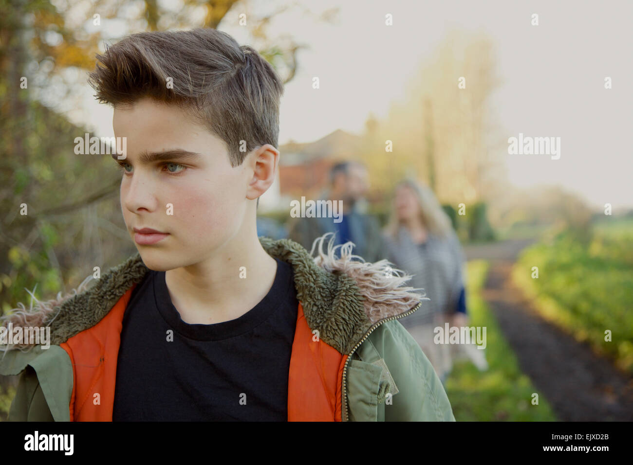 Teenage Boy Walking in Country Road, Parents in Background Stock Photo