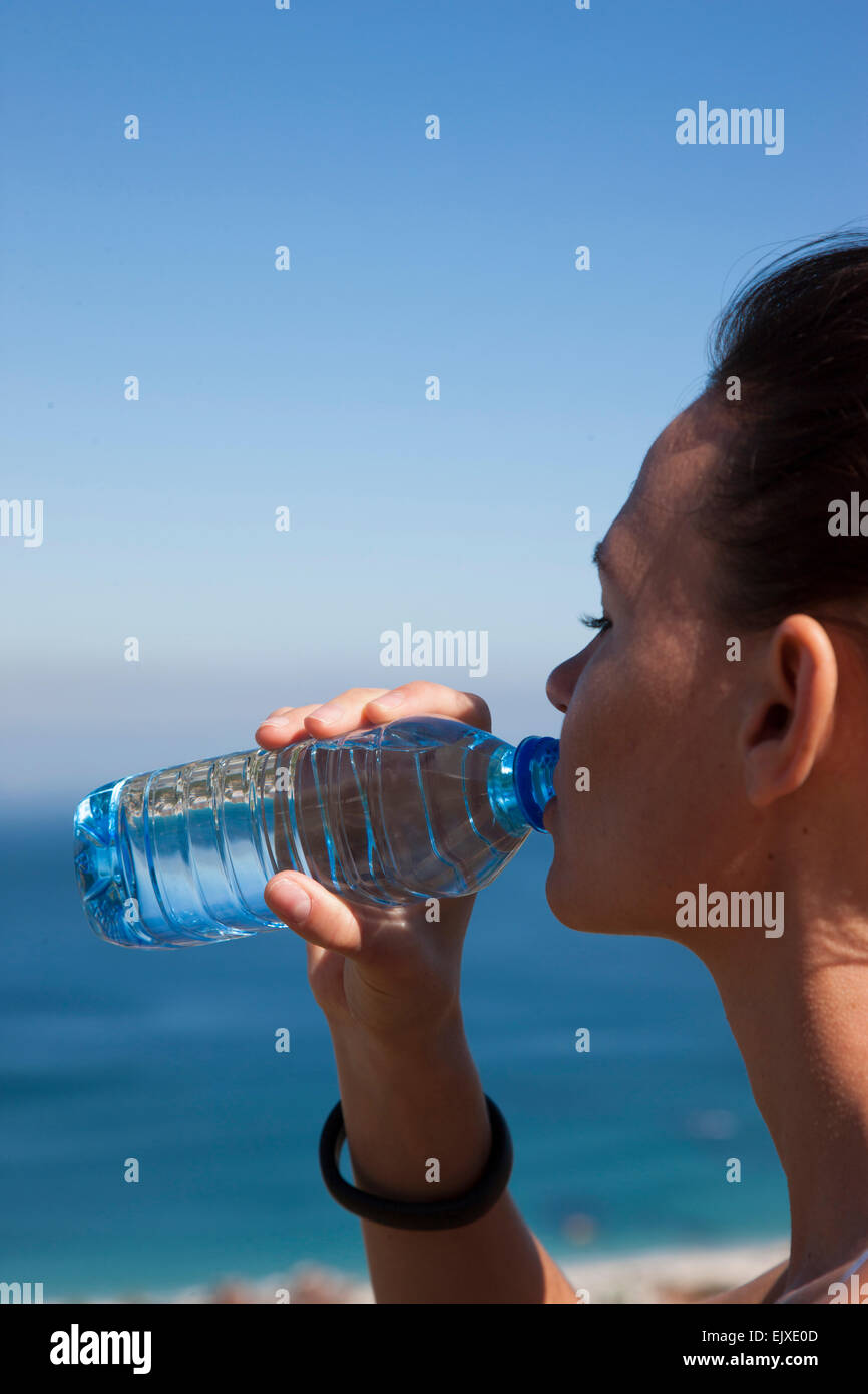 Woman Drinking Water from Bottle by Ocean Stock Photo