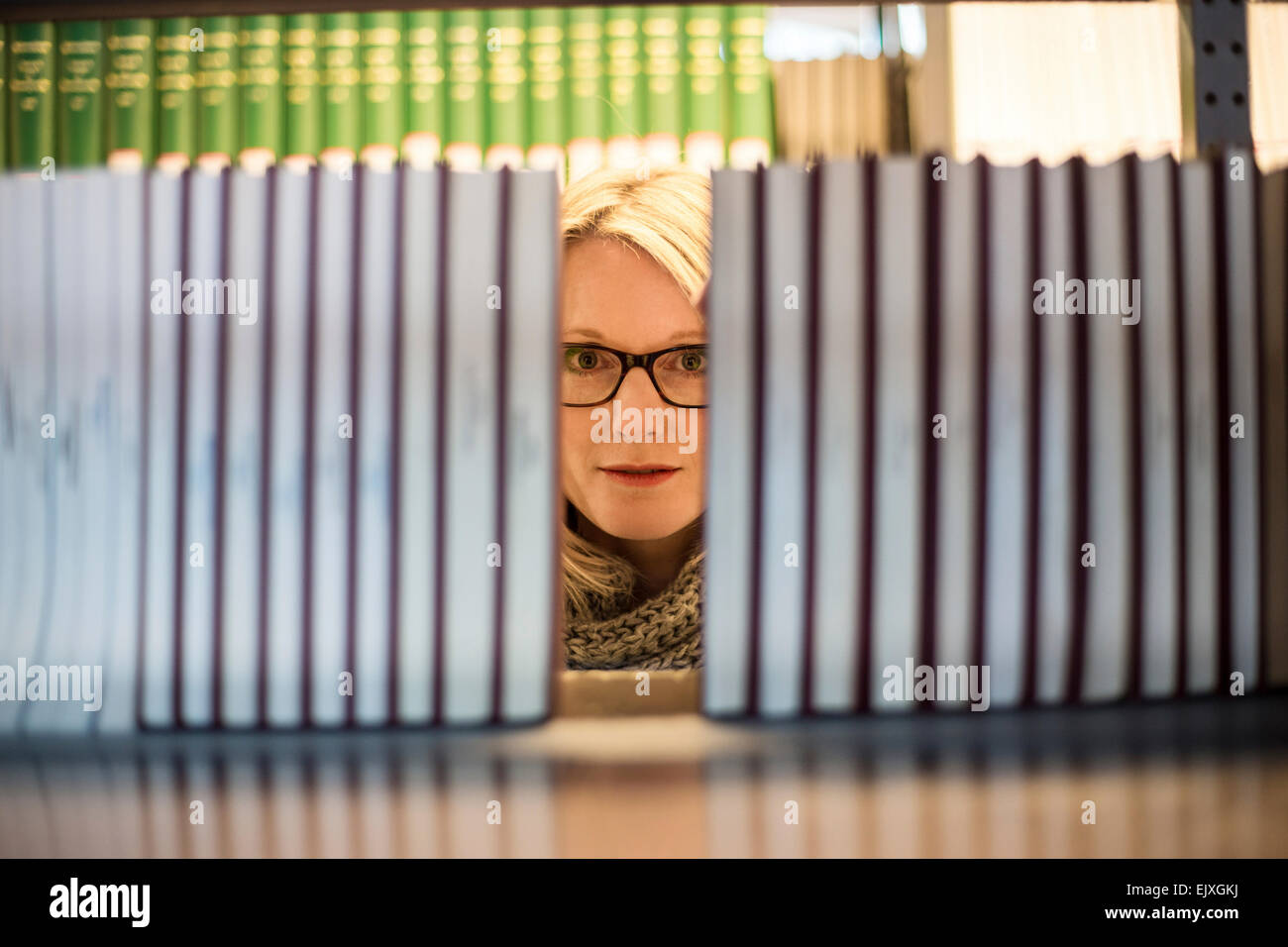 Woman in library looking from behind bookshelf Stock Photo