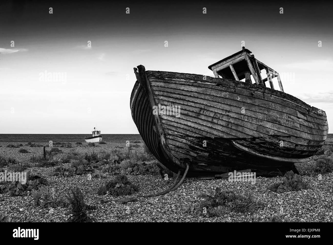 Abandoned fishing boat on shingle beach landscape at sunset black and ...