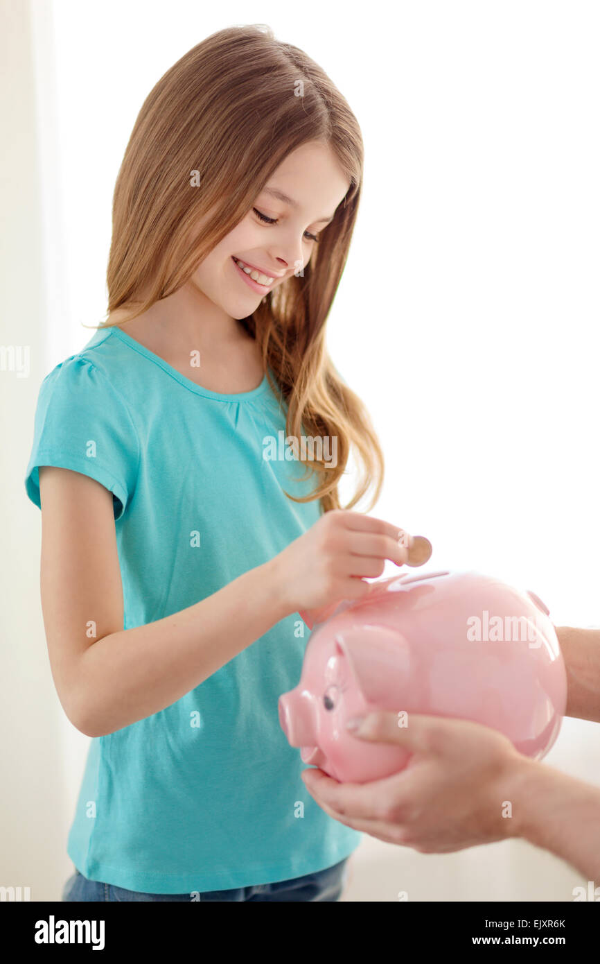 smiling little girl putting coin into piggy bank Stock Photo - Alamy
