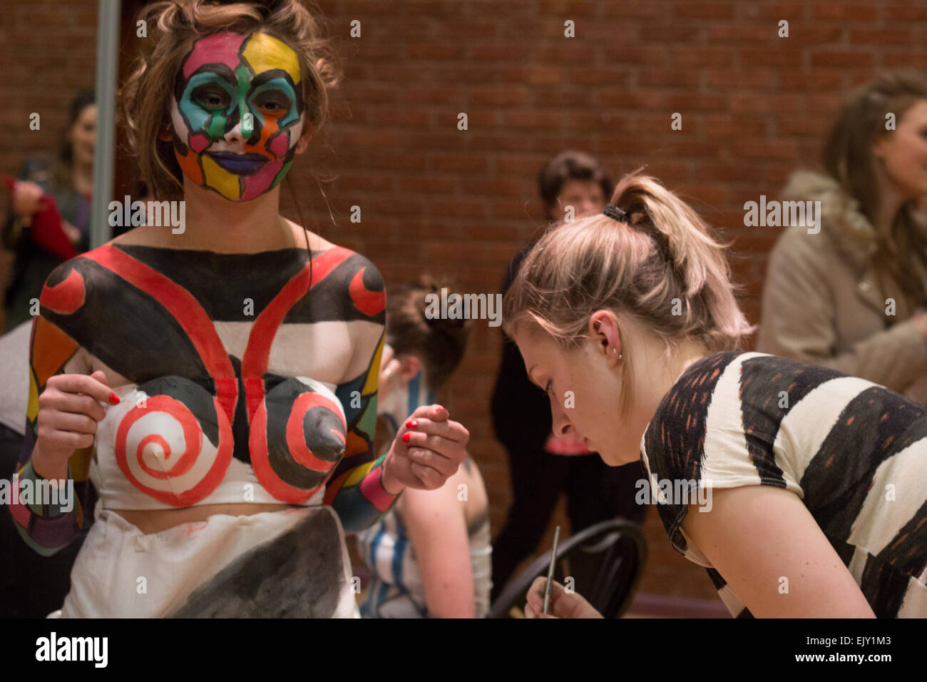Woman putting final touches of body paint onto a female model in costume and face paint. Stock Photo