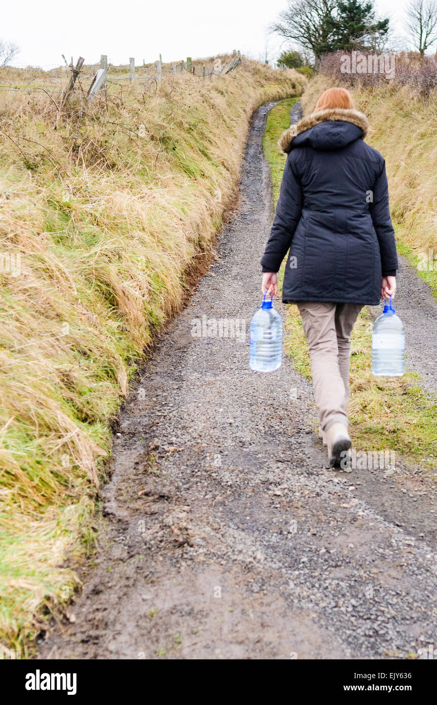 Woman carries bottled water home to a remote rural location after being without water supply Stock Photo