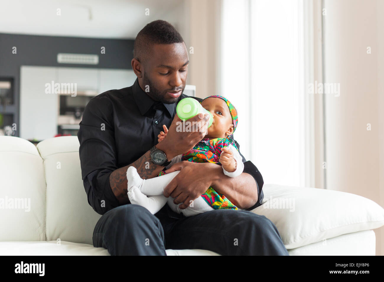 Young african american father giving milk to her baby girl in a