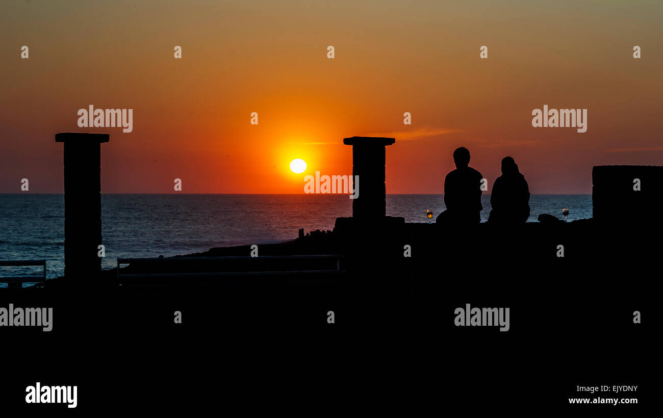 Atlantic Ocean , sunset . A man and a woman . Romantic evening on the  embankment. The sun is reflected in a glass with  wine. Stock Photo