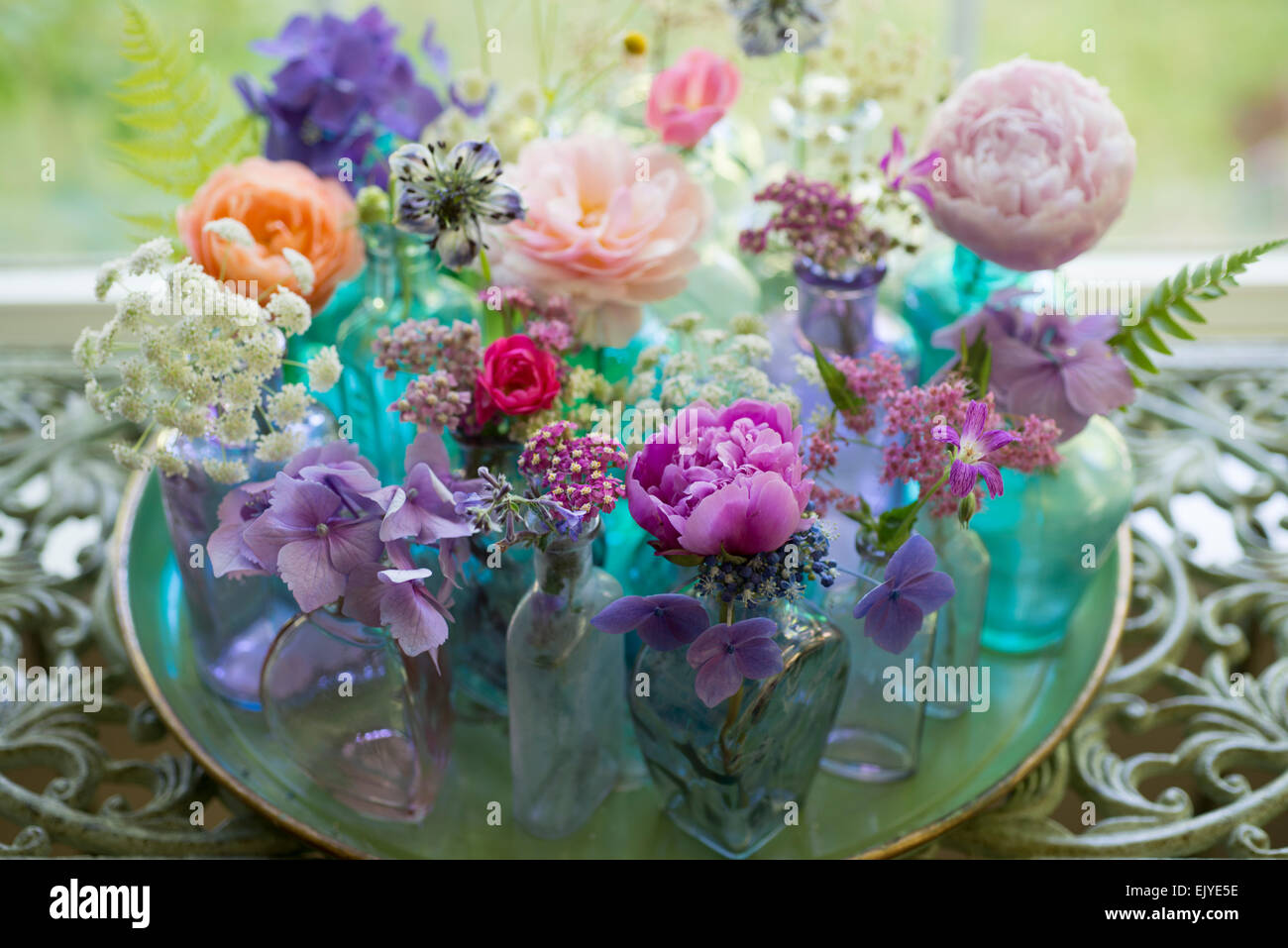 Floral arrangement of cut flowers in blue bottles including roses, hydrangea, peony, yarrow, feverfew and Queen Anne's Lace Stock Photo