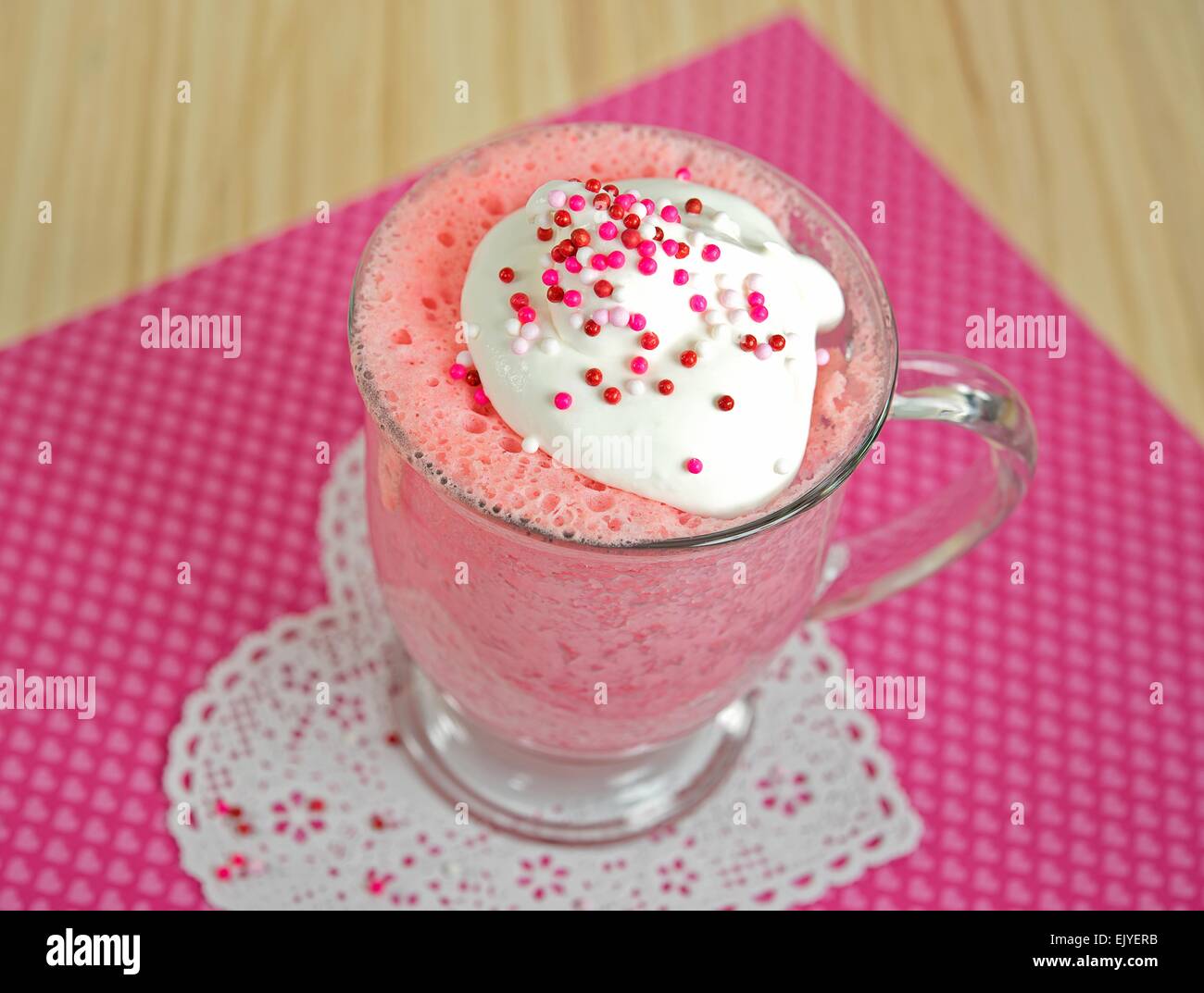 Pink cake in glass mug garnished with whipped cream and sprinkles on lace heart doily. Stock Photo