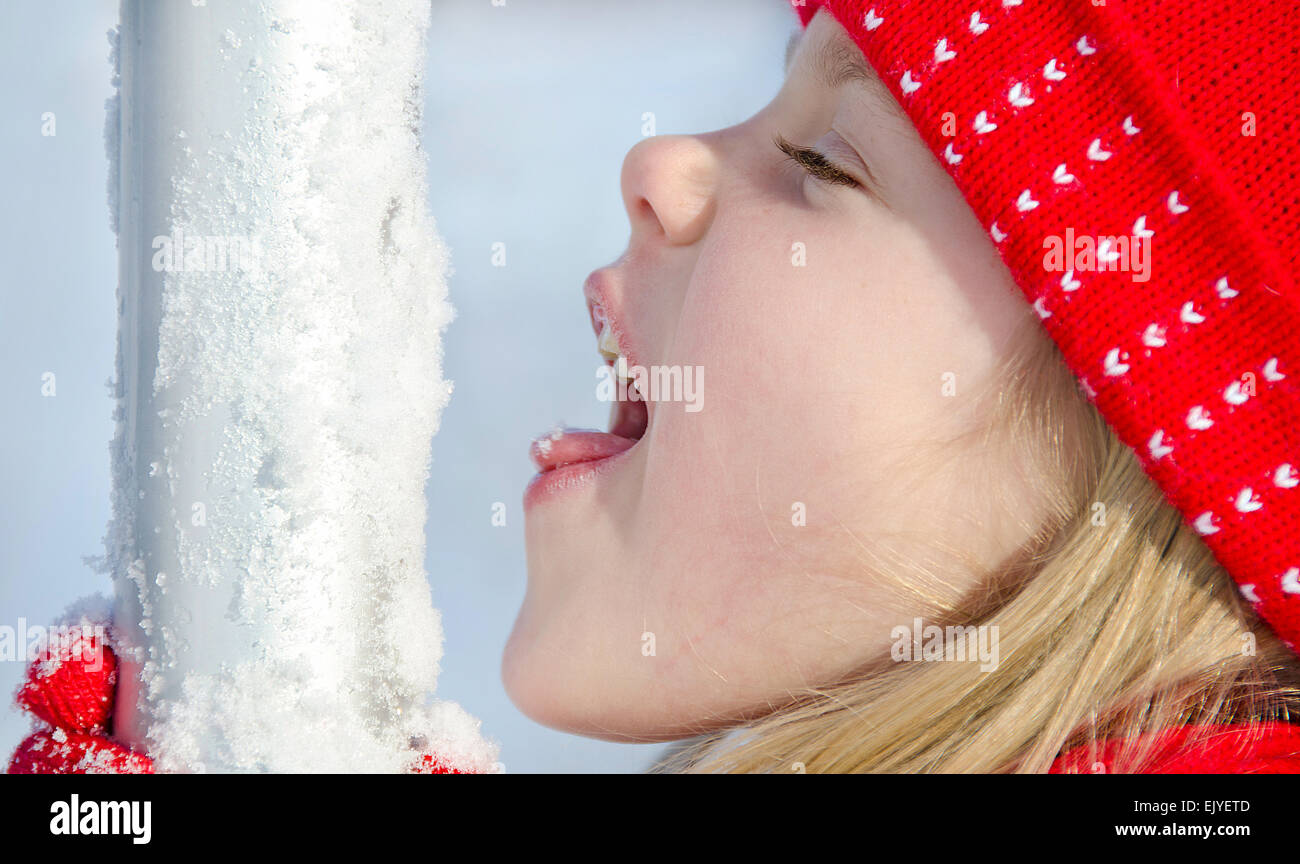 Little Caucasian girl liking snow off a flag pole. Stock Photo