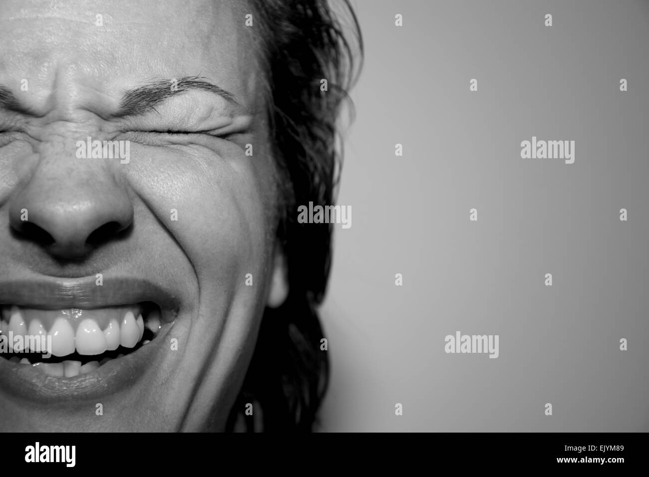 Closeup portrait of a pretty young woman laughing with closed eyes in monochrome indoors Stock Photo