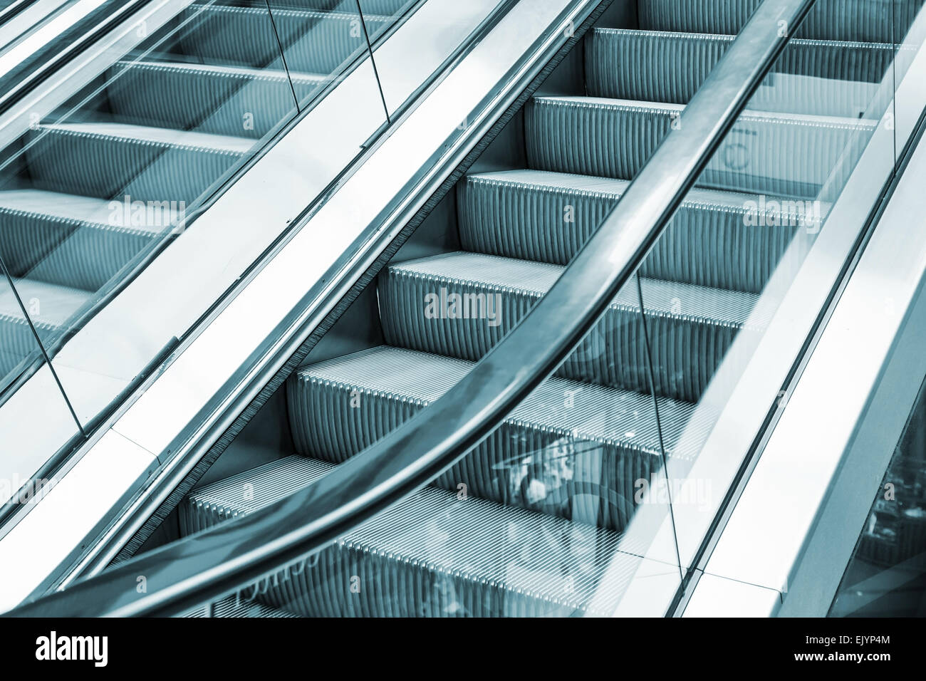 Shining metal escalator moving up, blue toned monochrome photo Stock Photo