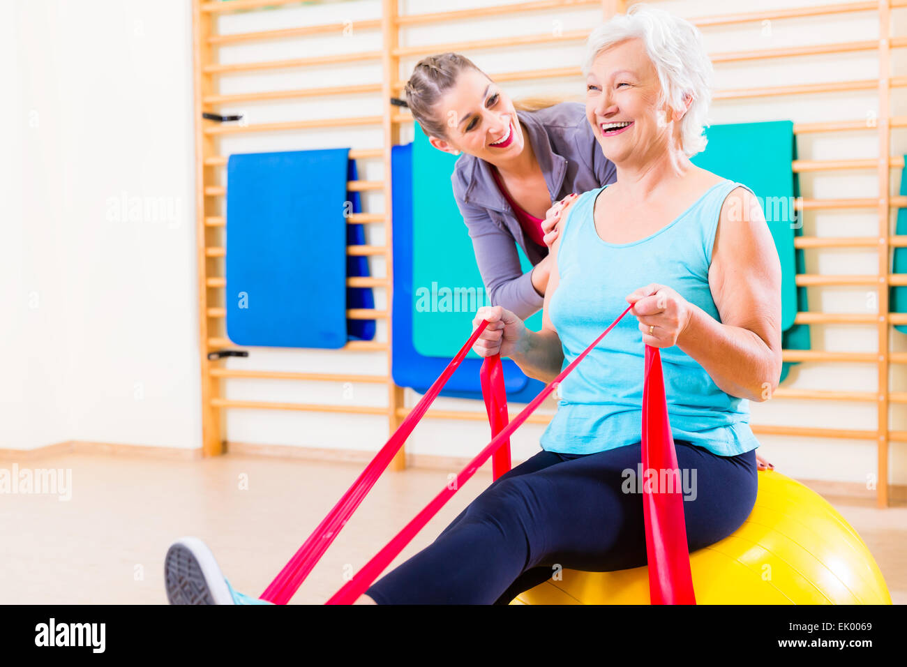 Senior woman with stretch band in fitness gym being coached by personal ...