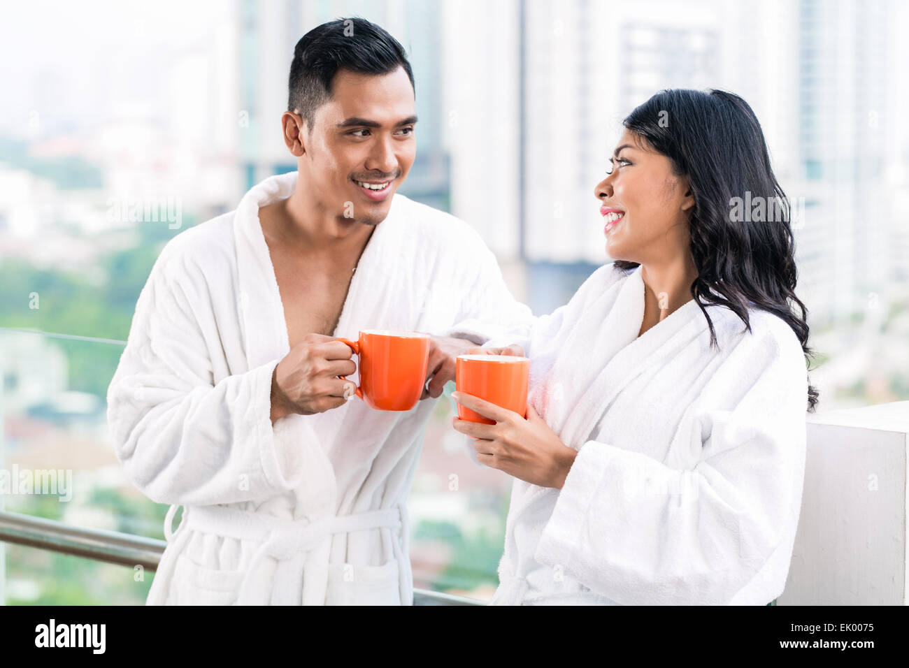 Asian couple in morning front of city skyline drinking coffee still in bathrobe Stock Photo