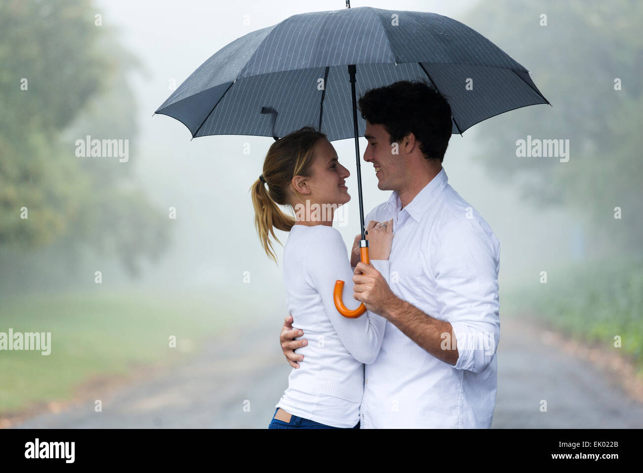 lovely young woman with boyfriend under an umbrella in the rain Stock Photo