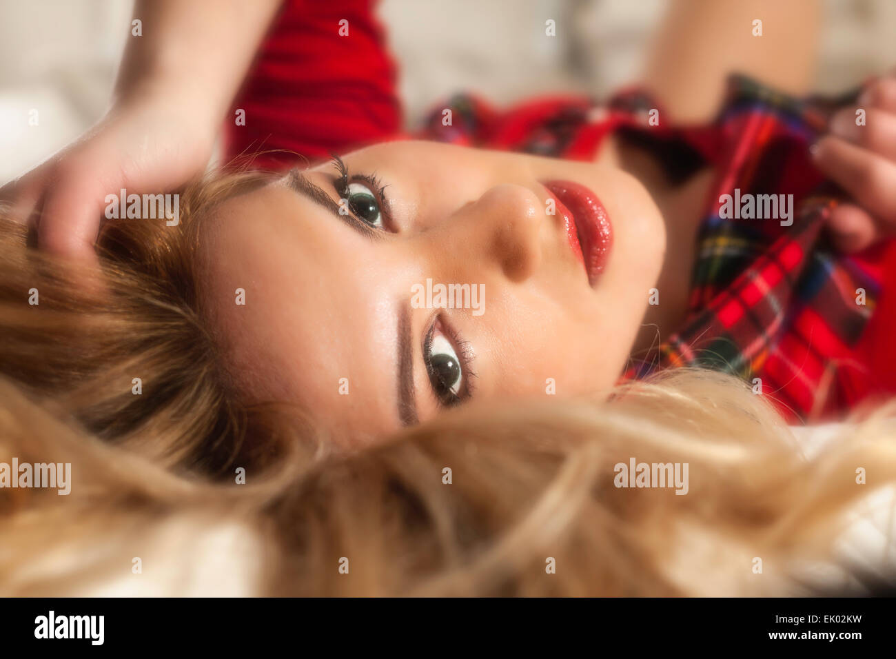 A closeup of a pretty blonde Latina girl with red lipstick laying on bed. Stock Photo