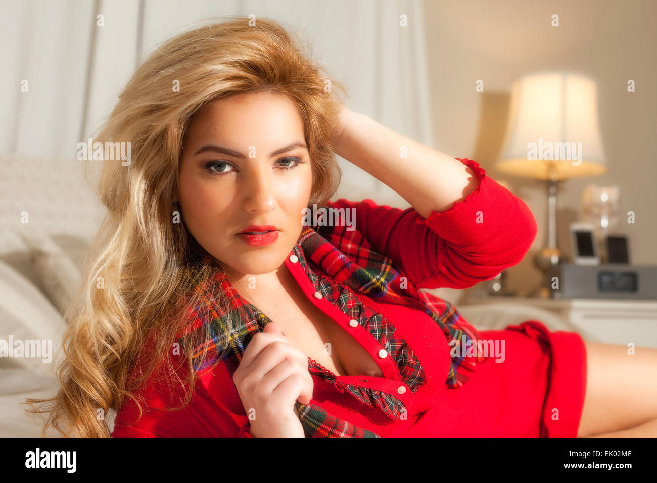 A pretty blonde Latina girl in red plaid Christmas clothes laying on her side with her hand in her big hair. Stock Photo