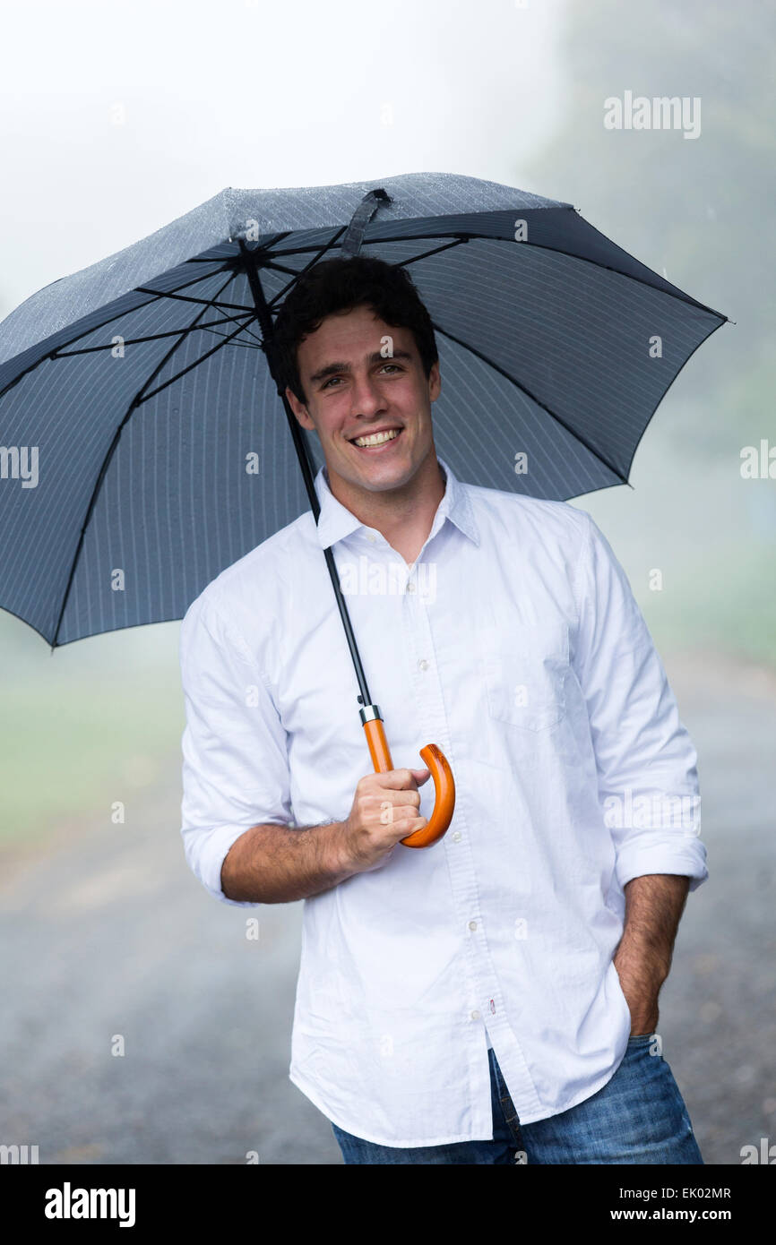 cheerful young man holding umbrella outdoors in the rain Stock Photo
