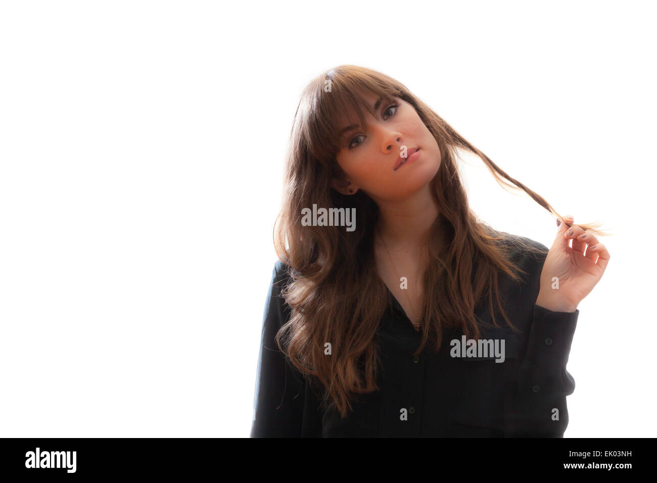 A pretty brunette model twirling her long hair between her fingers and biting her lip. Isolated on white background. Stock Photo