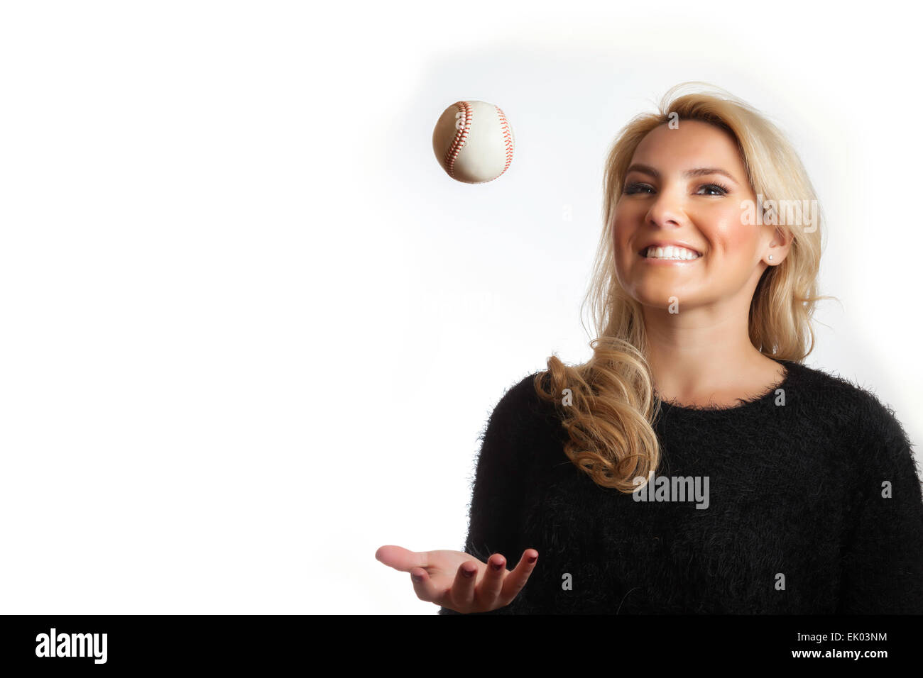 A pretty, Latina, blonde  in a black scarf tossing up and catching a baseball while smiling. Isolated on white background. Stock Photo