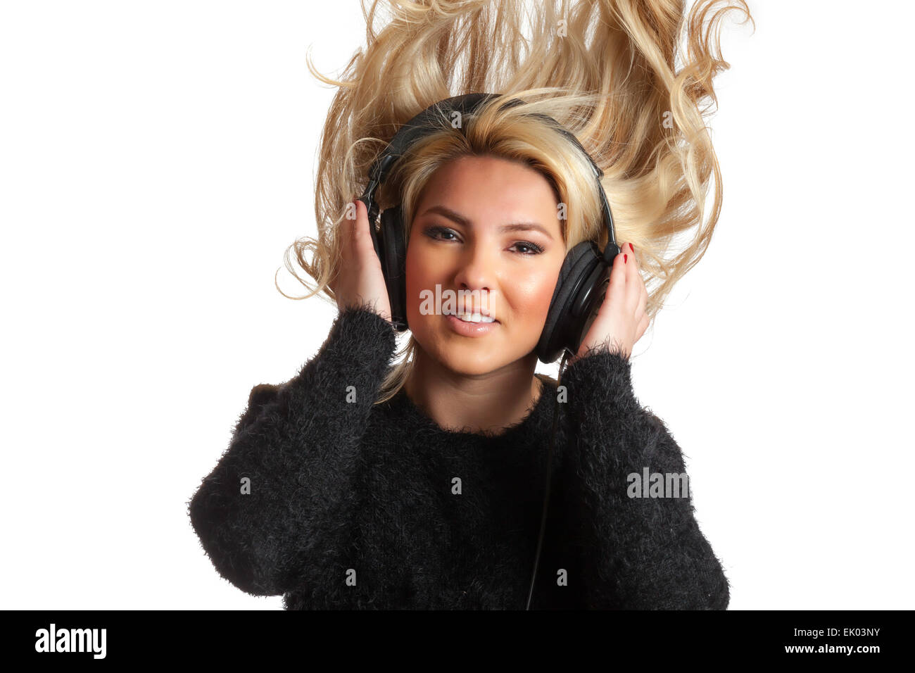 A pretty, blonde, Latina girl rocking out and flinging her hair while listening to large black studio headphones. Isolated on a  Stock Photo