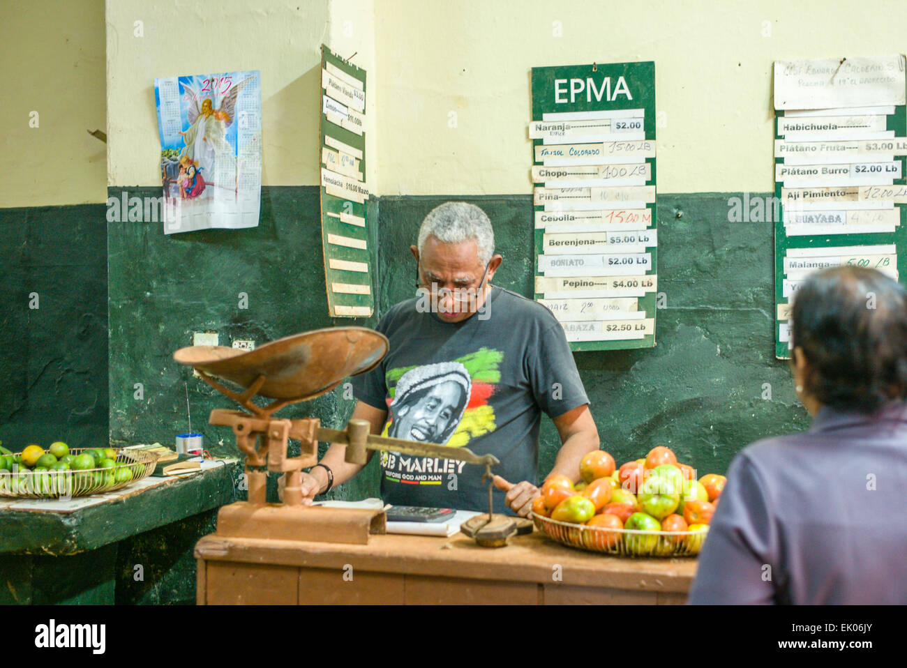 Government worker wearing a Bob Marly t-shirt weighs and prices fruit in CUP Cuban pesos for local buyers. Stock Photo