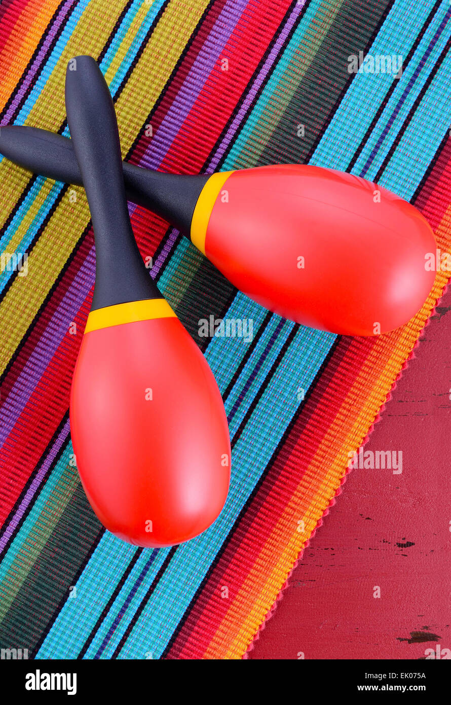 Happy Cinco de Mayo background with red and yellow maracas on Mexican style fabric and distressed red wood table. Stock Photo
