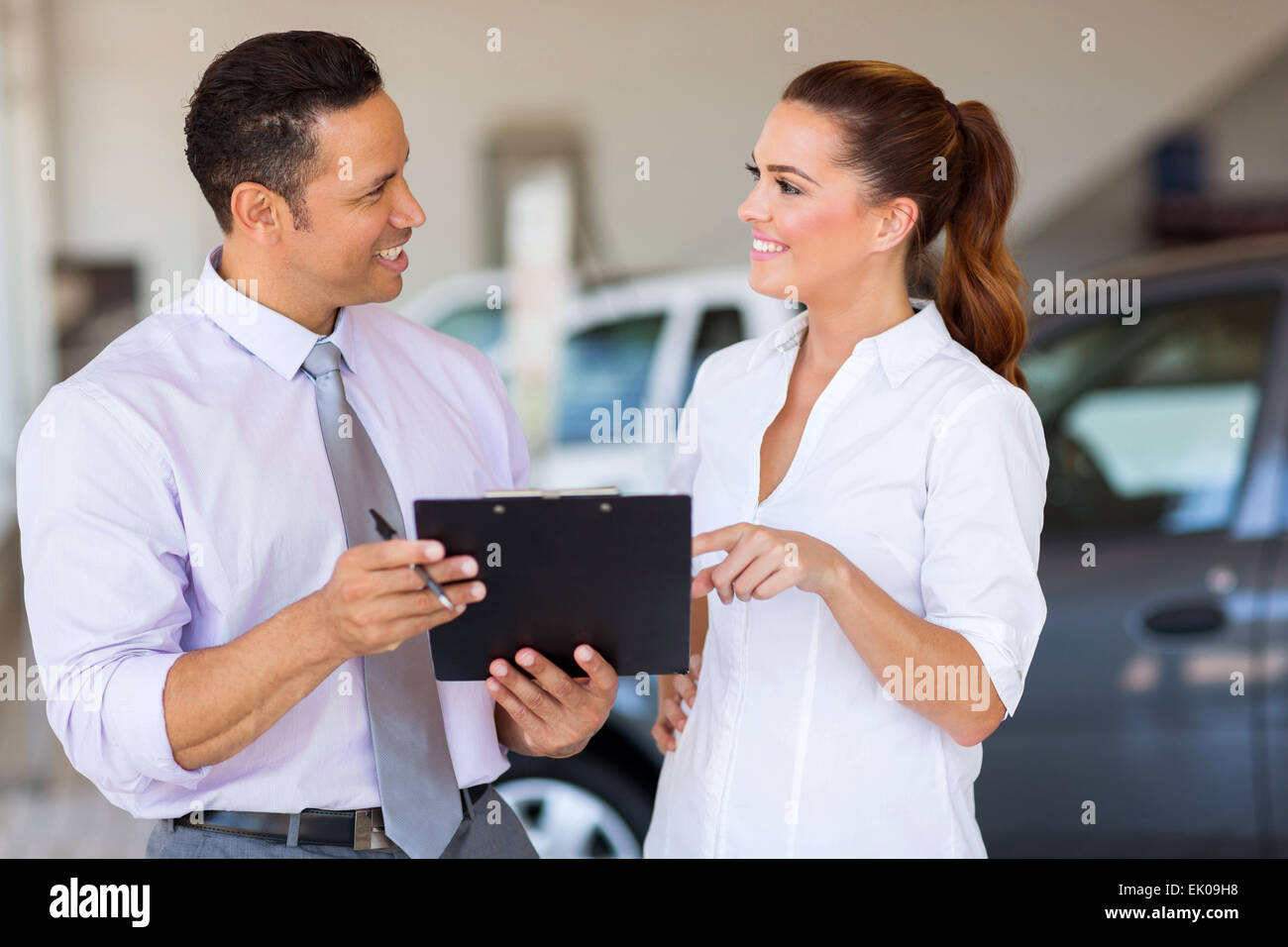 two happy car sales consultants working inside vehicle showroom Stock
