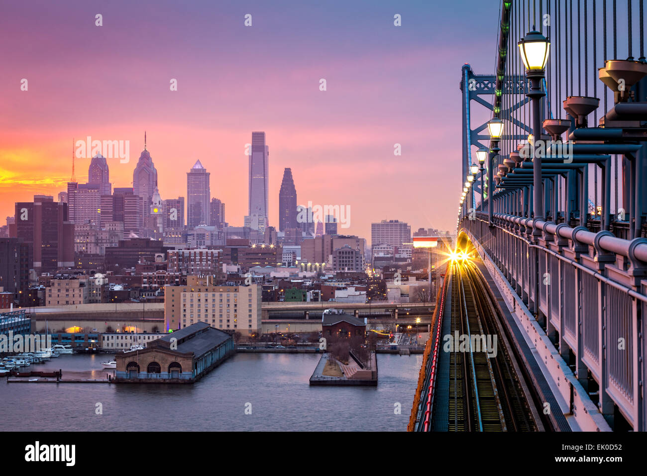 Philadelphia under a hazy purple sunset. An incoming train crosses Ben Franklin Bridge. Stock Photo