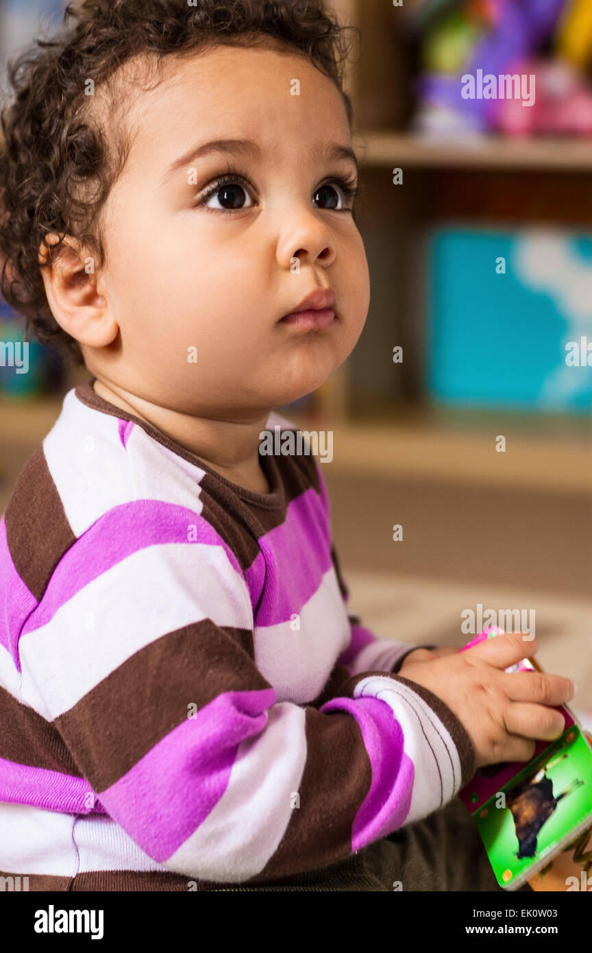 One year old baby girl sitting and holding a toy. Stock Photo