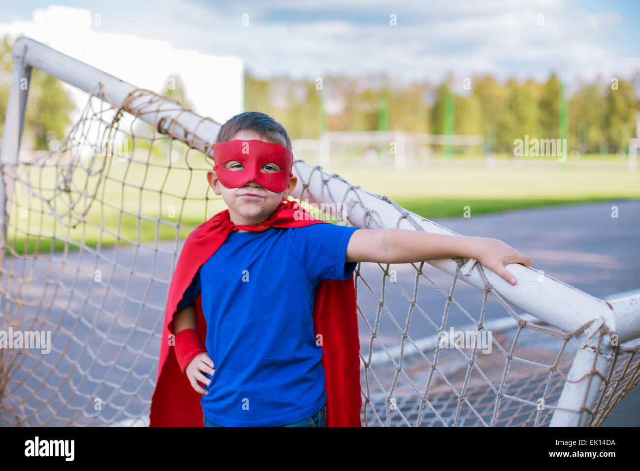 Boy dressed in cape and mask standing near football goal Stock Photo