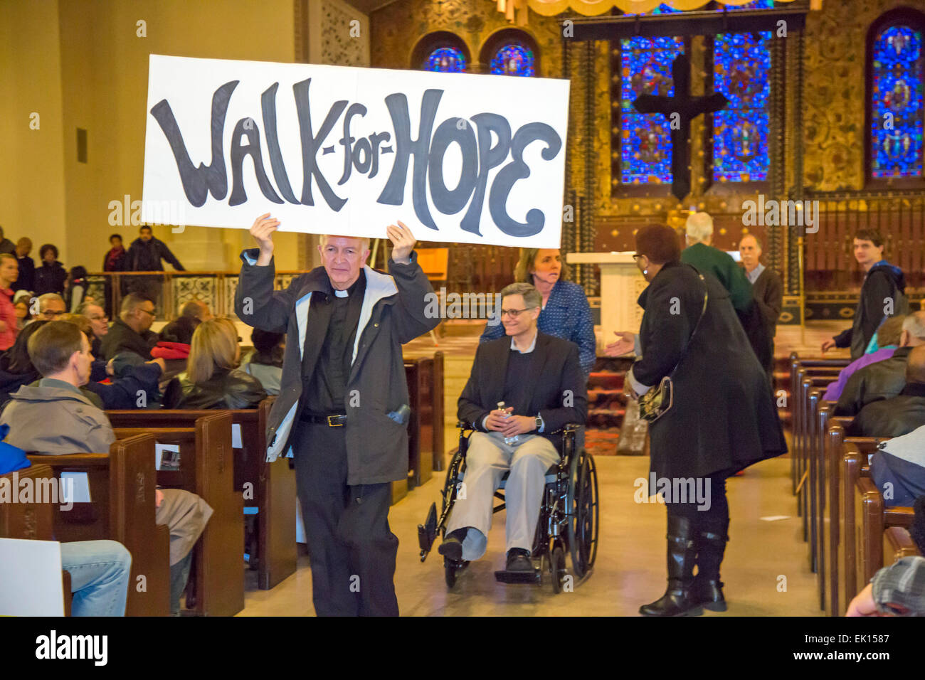 Detroit, Michigan USA - Members of Gesu Catholic Church and residents of the surrounding neighborhood joined in a Good Friday Peace Walk. The event was a reaction to the recent shooting of Federal Judge Terrence Berg, a member of the church and resident of the neighborhood, in an attempted robbery. Gesu Pastor Robert Sullin, S.J. leads the procession out of the church, followed by Berg in a wheelchair. Credit:  Jim West/Alamy Live News Stock Photo