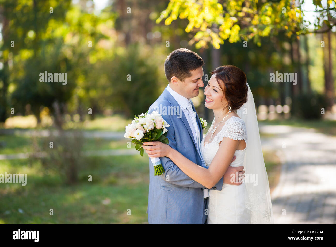 happy bride, groom standing in green park, kissing, smiling, laughing, embracing. lovers in wedding day Stock Photo