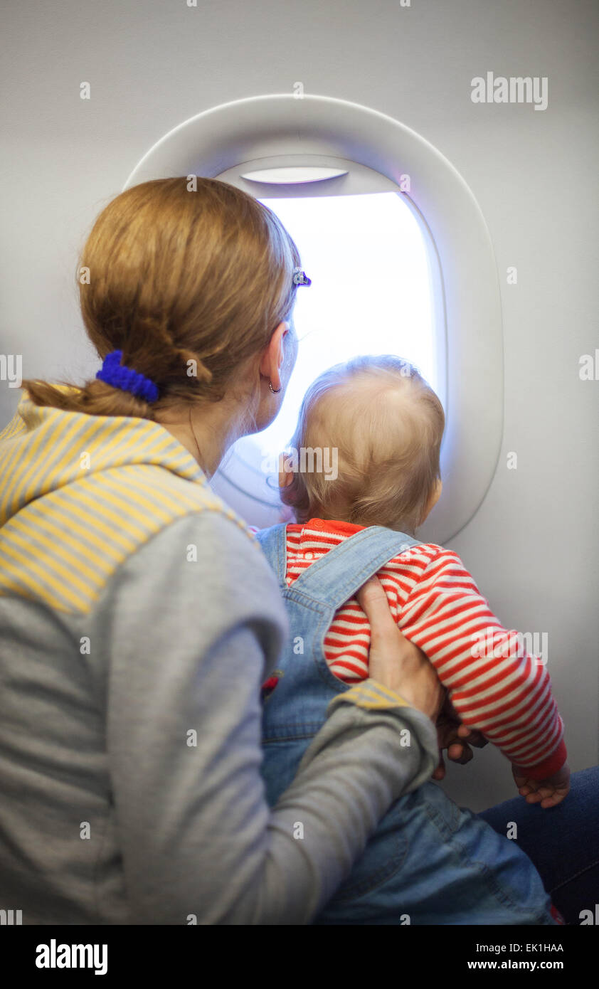 Mother and baby son looking out of window while on board of airplane Stock Photo