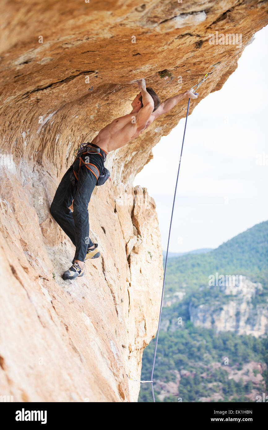 Young man clipping rope while clinging to cliff under ledge ...